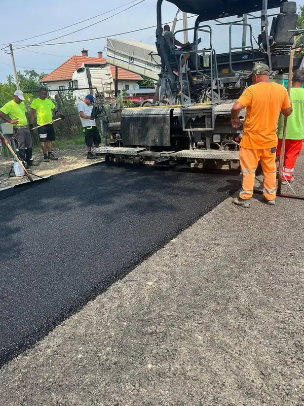 Aszfaltozó brigád finisherrel és kézi eszközökkel dolgozik utcán