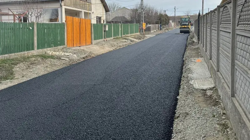 Frissen aszfaltozott falusi utca, a háttérben úthenger dolgozik